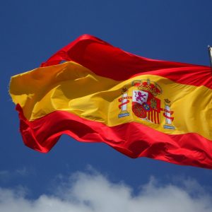 Vibrant Spanish flag waving against a clear blue sky and clouds.